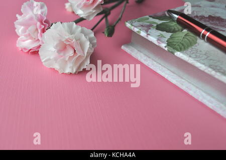 Pink background with carnations, notebook and pen with copy space. Stock Photo