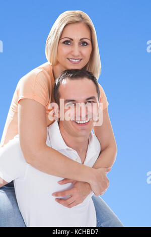 Happy Man Piggybacking His Girlfriend Against Blue Sky Stock Photo