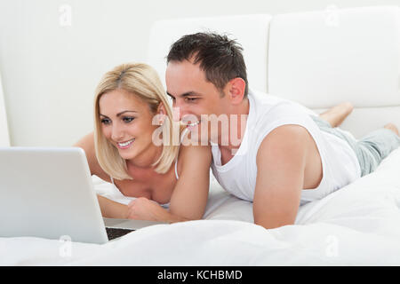 Happy Couple In The Bedroom Using Laptop Stock Photo