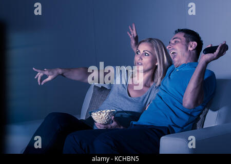 Scared Couple Watching Horror Movie At Home Stock Photo