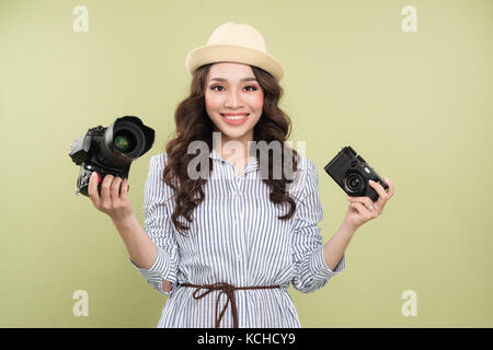 Young asian woman comparing professional and compact cameras on green background Stock Photo