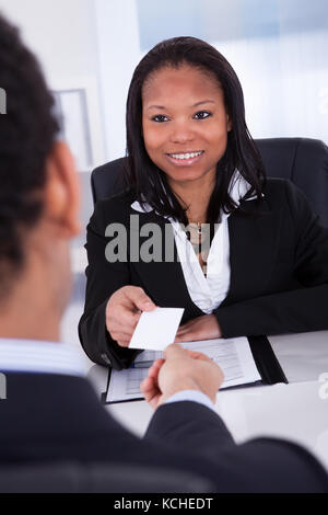 Businesswoman Offering Visiting Card To Man In Office Stock Photo