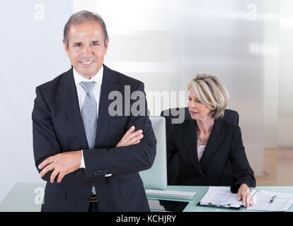 Happy Businessman Standing In Front Of His Colleague Using Computer Stock Photo