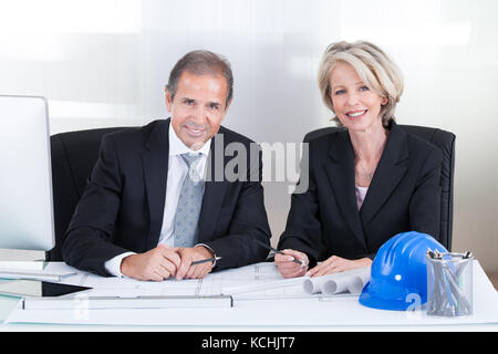 Mature Engineers Looking At Plans Sitting At A Table Stock Photo