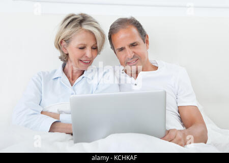 Portrait Of Happy Mature Couple On Bed Using Laptop Stock Photo