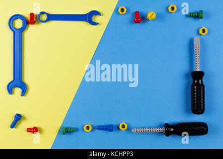 Toys background. Kids construction toys tools frame with screwdrivers, screws and nuts on blue and yellow background. Stock Photo