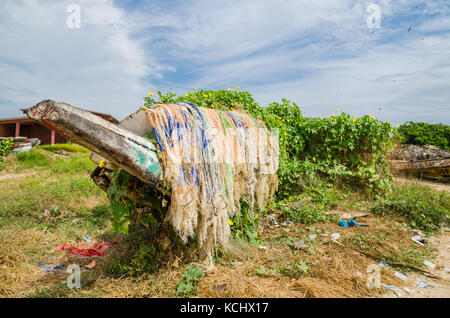 Colorful overgrown and broken wooden fishing boats with nets and traps in lush environment, coast of Gambia, West Africa Stock Photo