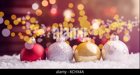 Multi colored baubles lined up on snow against Christmas tree Stock Photo