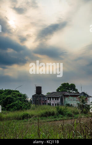 Ruined mansion surrounded by lush green with dramatic sky. Traces of the civil war in Robertsport, Liberia Stock Photo