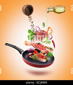 Fresh vegetables with pieces of beef meat, spices and oil flying into a pan. Stock Photo