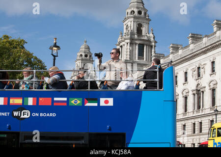 Tourist taking photographs on top deck of  open top double decker London bus Westminster Stock Photo