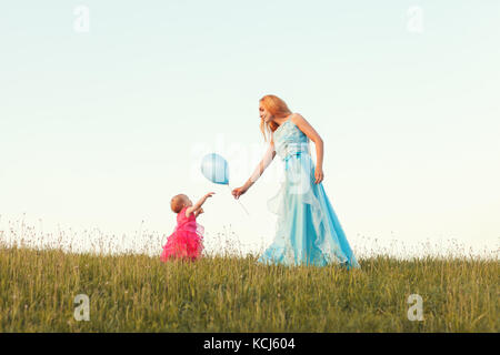 Young blonde woman giving her daughter a balloon Stock Photo