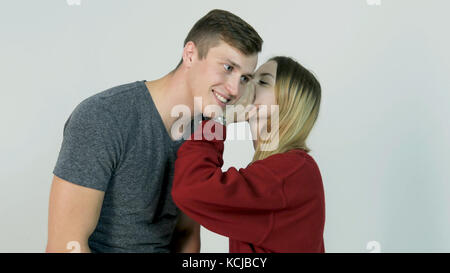 Pretty girl whispering secret in ear of her laughing friend on white background - friendship concept Stock Photo