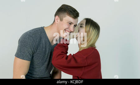 Pretty girl whispering secret in ear of her laughing friend on white background - friendship concept Stock Photo