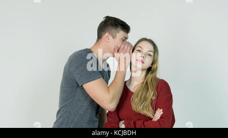 Pretty girl whispering secret in ear of her laughing friend on white background - friendship concept Stock Photo