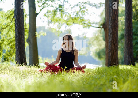 young woman in red skirt enjoying meditation and yoga on green grass in the summer on nature Stock Photo