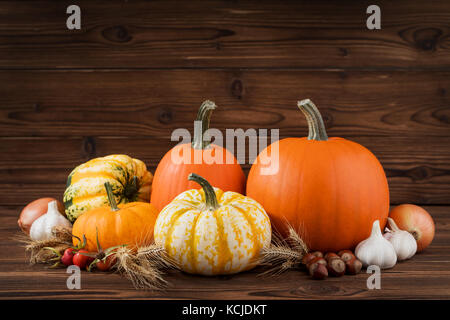 Autumn harvest still life with pumpkins, wheat ears, hazelnuts, garlic, onion and rosehip berries on wooden background Stock Photo