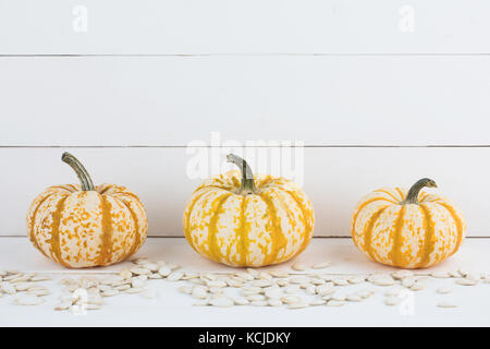 Three orange pumpkins and seeds on white wooden background, Halloween concept Stock Photo