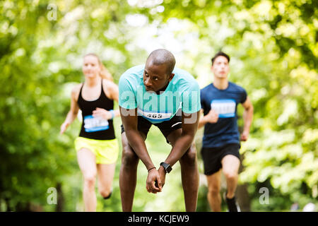 Group of young athletes running a race in green sunny park. Stock Photo