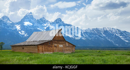 The T. A. Moulton barn sits in a grassy field beneath the Grand Teton mountains in Wyoming Stock Photo