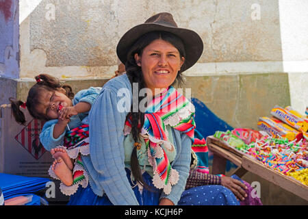 Cholita, Bolivian woman with hat and long black hair braid carrying child on her back in the town Tarabuco, Chuquisaca, Yamparáez Province, Bolivia Stock Photo