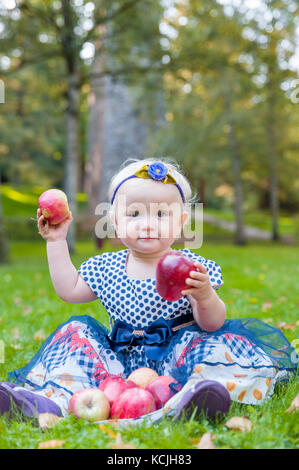 Baby girl sitting on the grass and playing with her apples Stock Photo