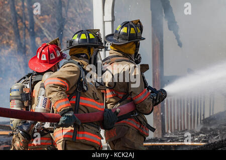 Firemen wearing their full structural firefighting kits battle flames of unknown origin at a house fire in Lisbon, NH, USA on Oct 5, 2017. Stock Photo