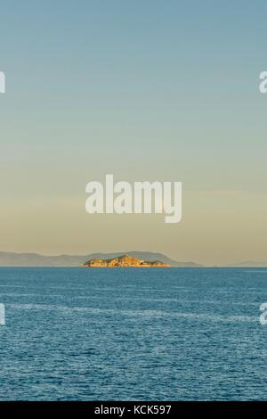 Vertical photo with evening view on the rock in Mediterranean Sea between elba island and Italian coast. The sky is almost clear and blue with the moo Stock Photo