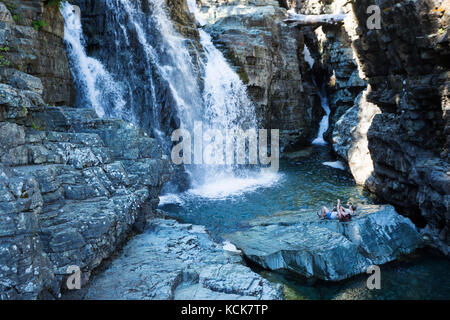 Two friends relax on an outcropping of rock at the bottom of Lower Myra Falls in Strathcona Park, Vancouver Island, British Columbia, Canada Stock Photo