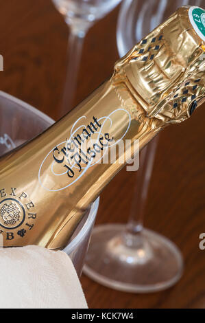 Cremant d’Alsace sparkling wine bottle in ice bucket with glasses behind on dining table Stock Photo