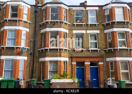 Facade of an Edwardian restored residential tenement building in red and yellow bricks with classic bay windows and blue entrance doors. Stock Photo