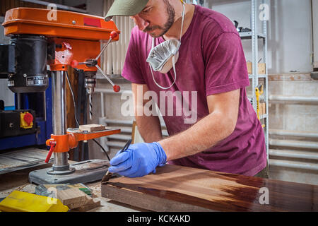 A man in a work shirt and green merchandise paints a wooden brush with a wooden brush for protection against corrosion in the workshop, in the backgro Stock Photo