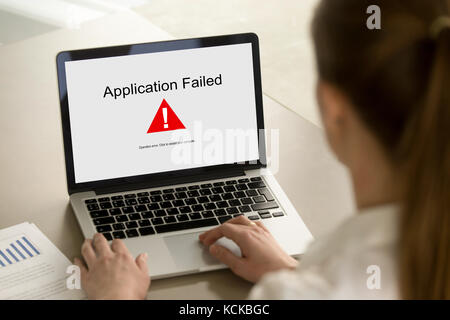 Girl looking at laptop with Application Failed error on screen. App stopped working, software failure, computer unit broke, system crashed unexpectedl Stock Photo