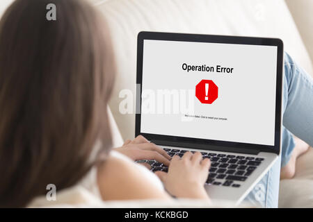 Woman lying on sofa looking at laptop screen, Operation Error message pop up. Computer crashed, software failure during web browsing, watching movie,  Stock Photo