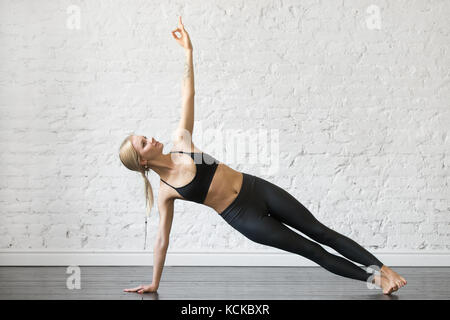 Young attractive woman practicing yoga, standing in Side Plank exercise, Vasisthasana pose, working out, wearing sportswear, black top and pants, indo Stock Photo