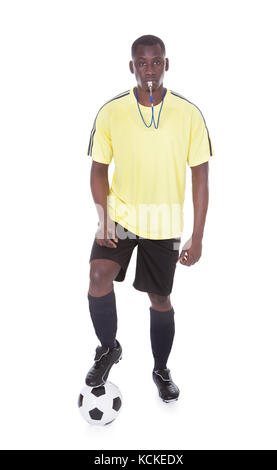 Soccer Referee Blowing Whistle With Leg On Ball Over White Background Stock Photo