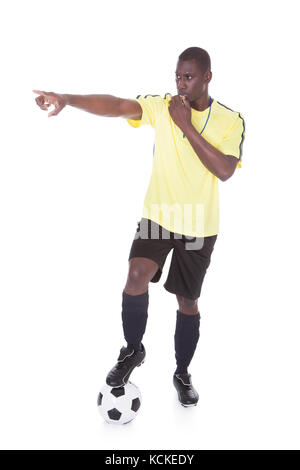 Soccer Referee Blowing Whistle With Leg On Ball Over White Background Stock Photo