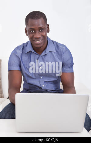 Portrait Of Happy African Man Using Laptop In Living Room Stock Photo