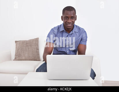 Portrait Of African Man Sitting On Couch Using Laptop Stock Photo
