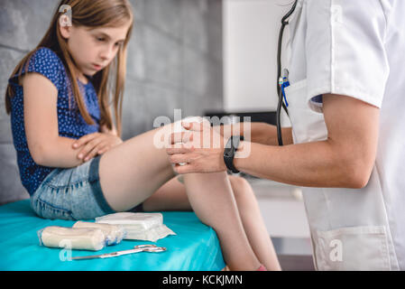 Medical female doctor bandaging young girl knee at the hospital Stock Photo