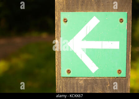 White arrow on green background turn left sign on wooden post with greenery foliage bokeh Stock Photo