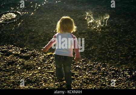 Toddler, girl around three years old throwing stones in river. Mersey River, Tasmania, Australia Stock Photo