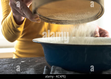 White flour is sieved in a large blue bowl horizontal Stock Photo