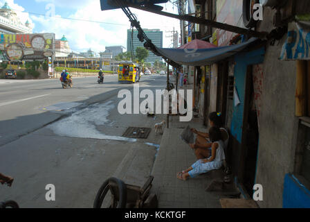 Mother reading a newspaper whilst sat on pavement with her daughter, Cebu, Philippines. Stock Photo