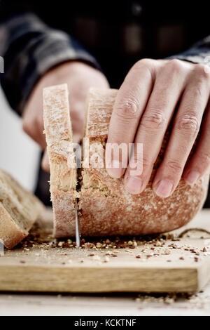 closeup of a young caucasian man cutting a spelt bread roll in slices with a knife Stock Photo