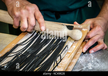Head chef José Graziosi presses a sheet of squid-ink pasta dough through the wires of the carraturo with a rolling pin, cutting it into thin strips, in the kitchen of Hotel Endsleigh in West Devon, England. The dough is first rolled several times through a pasta machine until thin, then briefly floured and cooked in salted water until al dente. Salvatore Piacente, who like Graziosi trained at the Santa Maria cooking school in Italy's Abruzzo region, assists at his side. Stock Photo