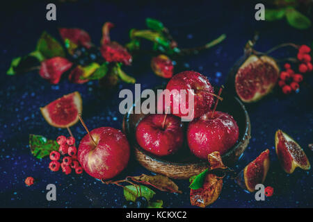 Ripe sweet apples in a wooden plate close-up in an autumn still life with fallen leaves. Autumn harvest scene. Dark food photography with copy space.  Stock Photo