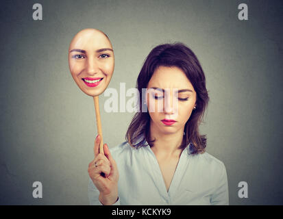 Sad woman looking down taking off happy mask of herself Stock Photo