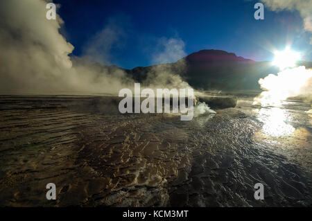 Chile Atacama Desert. Geyser del Tatio( 4.300 m.). decine di piccoli geyser, solfatare, pitte di fango e soffioni costellano questo altipiano.All'alba le colonne di vapore sono molto alte| Chile Atacama Desert tens of small geysers, fumaroles, mud pitts are all around this magnificient high plateau. At sun rise, the vapor collums are a lot higher. Waiting the sun rise while the moon sets. Stock Photo