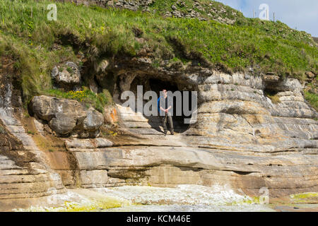 Man stood at a cave entrance at the north end of the Bay of Laig on the Isle of Eigg, Scotland, UK Stock Photo